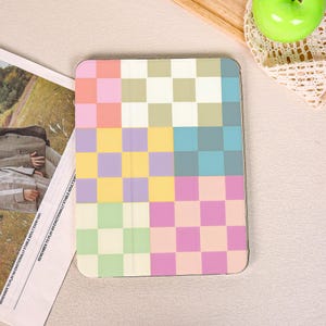 May include: A multi-colored tablet case with a checkerboard pattern in pastel shades of pink, yellow, green, and blue. The case is rectangular and has a smooth surface. The text "REMEMBER TO PLAY AN EMOTIONALLY STABLE ADULT EVERY DAY" is visible on a nearby paper.