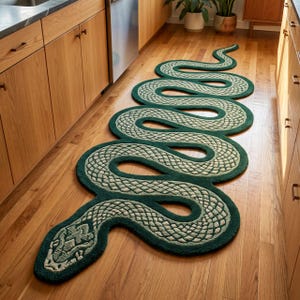 Puede incluir: Una alfombra larga con forma de serpiente que presenta un borde verde bosque profundo y un interior verde salvia más claro con un patrón de escamas detallado y repetitivo. La alfombra tiene una forma sinuosa que se extiende por el suelo.
