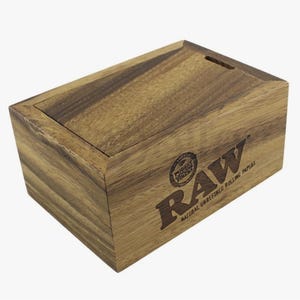 K&ouml;nnte beinhalten: Rechteckige Holzbox mit Schiebedeckel aus hellbraunem Holz. Auf der Vorderseite befindet sich das "RAW"-Logo und der Text. F&uuml;r nat&uuml;rliche, unraffinierte Zigarettenpapiere.