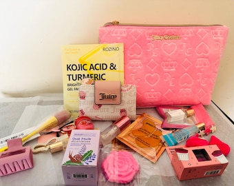 May include: An assortment of beauty products and accessories, including a pink Juicy Couture cosmetic bag, skincare items, makeup brushes, and a small wallet. The items are arranged on a white surface, with a variety of colours and textures.