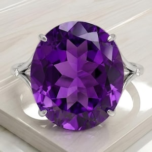 Può includere: Anello in argento con una grande ametista ovale. La pietra viola scuro è incastonata in una fascia d'argento con piccole pietre di accento. L'anello è esposto su una superficie bianca.