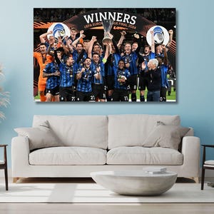 Può includere: Stampa su tela incorniciata di una squadra di calcio che festeggia una vittoria, tenendo in mano un trofeo. La squadra indossa maglie blu e nere. Le parole "WINNERS" e "UEFA EUROPA LEAGUE FINAL 2024" sono visibili.