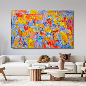 May include: Abstract art painting with a vibrant mix of colors, including red, yellow, blue, and orange. The artwork is displayed above a white sofa in a modern living room setting. The painting's brushstrokes create a textured appearance.