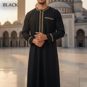 May include: Black long-sleeve garment with gold embroidery around the collar, pocket, and cuffs. The word "BLACK" is in the upper left corner. The garment is worn by a person in front of a building with arches.