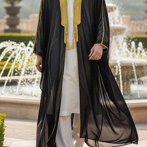 May include: Black open-front robe with gold trim and tassels, worn over a white tunic and pants. The robe has a sheer, flowing design. The word "BLACK" is in the top left corner. The outfit is suitable for special occasions.