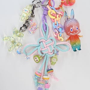 Peut inclure: Un assortiment de porte-clés et de breloques colorés. Les porte-clés comprennent un chien ballon transparent, un charm en forme de cœur rempli de paillettes et une figurine arc-en-ciel. Les breloques présentent divers motifs, dont un lapin et un personnage de dessin animé.