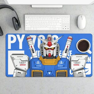 May include: Blue rectangular desk mat featuring a detailed illustration of a Gundam robot. The robot is primarily blue, white, yellow, and red, with the text "PY 700" and other text. A white coffee cup and computer accessories are also visible.