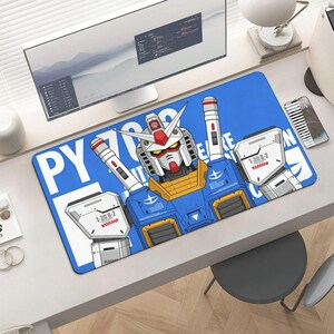 May include: A blue rectangular mousepad featuring a detailed illustration of a robot character with white, red, yellow, and blue accents. The mousepad has white text on the left side and the top. The mousepad is on a white desk.