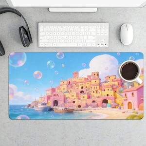 May include: A rectangular mouse pad featuring a vibrant illustration of a coastal town with pink and yellow buildings, boats, and bubbles against a blue sky. A white coffee cup sits on the pad, near a keyboard and mouse.