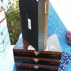 May include: A stack of five wooden cigar boxes with black lids. The boxes are labeled "1935 - Anniversary" and "10 Toro". The top box is labeled "Montecristo" and has a number "4620" on it.