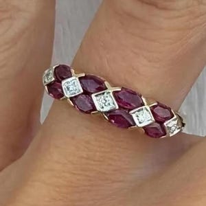 Peut inclure: Une bague en or ornée d'un motif répétitif de rubis rouge foncé taille marquise alternant avec de petits diamants clairs taille carrée. Les pierres sont serties en une rangée continue sur le dessus de l'anneau, créant un design texturé.