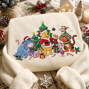 Può includere: Una felpa color crema con un ricamo raffigurante Winnie the Pooh, Ih-Oh, Tigro e Pimpi che festeggiano il Natale. I personaggi sono riuniti attorno a un albero di Natale decorato con regali, fiocchi di neve e bastoncini di zucchero.