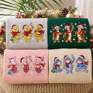 Può includere: Quattro felpe piegate in grigio, verde scuro, rosa chiaro e beige. Ognuna presenta un trio di personaggi di Winnie the Pooh con cappelli da Babbo Natale e sciarpe, avvolti in luci natalizi colorate e bastoncini di zucchero.