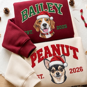 Pode incluir: Uma camisola bordeaux com um beagle bordado a usar um gorro de Pai Natal e o texto BAILEY EST. 2025, e uma camisola creme com um chihuahua bordado a usar um gorro de Pai Natal e o texto PEANUT EST. 2026 em letras vermelhas.