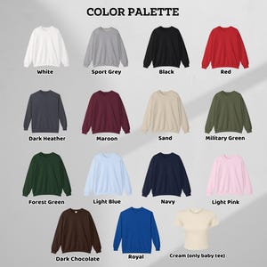 May include: A color palette chart displaying fourteen crewneck sweatshirts and one short-sleeve baby tee in various colors including white, sport grey, black, red, dark heather, maroon, sand, military green, forest green, light blue, navy, light pink, dark chocolate, royal, and cream.