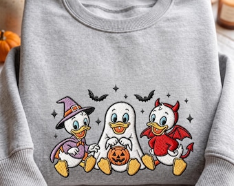 Puede incluir: Una sudadera gris jaspeado de cuello redondo con un diseño bordado de tres patos de dibujos animados disfrazados para Halloween. Un pato lleva un sombrero de bruja y capa morada, otro va de fantasma blanco con una calabaza y otro de diablo rojo.