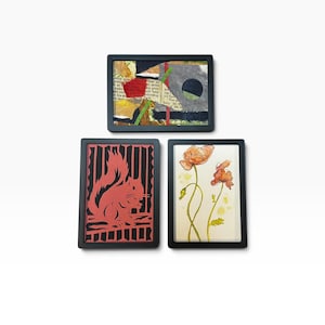 May include: Three framed artworks with black borders. The top piece is a collage of newspaper clippings and abstract shapes. The bottom left piece features a red paper-cut silhouette of a squirrel. The bottom right piece shows watercolor poppies.