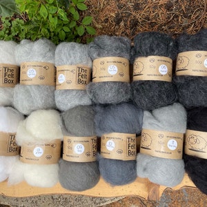 May include: Ten skeins of wool yarn in various shades of gray, white, and black. Each skein is labeled with "The Felt Box" and a number from 03 to 08. The skeins are arranged in two rows of five on a wooden surface.