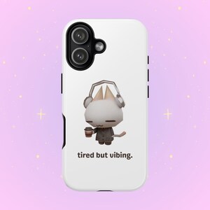 Peut inclure: Coque de téléphone blanche avec un personnage de chat de dessin animé portant un casque et tenant une tasse de café. Le texte "tired but vibing" est imprimé en dessous. Le boîtier a des boutons latéraux noirs et des objectifs d'appareil photo.