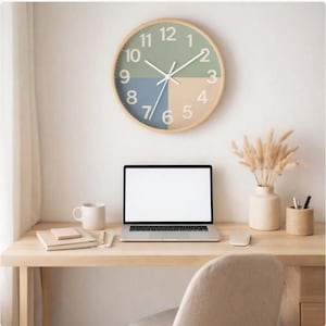Könnte beinhalten: Eine runde Wanduhr mit hellem Holzrahmen und einem segmentierten Zifferblatt in Grün, Blau und Beige. Die Uhr ist an einer weißen Wand über einem Holzschreibtisch mit Laptop, Becher und dekorativen Gegenständen angebracht.