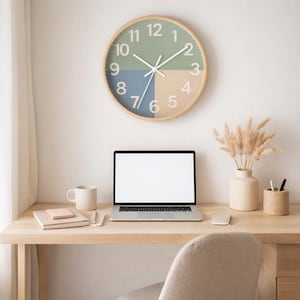 May include: A wooden-framed wall clock with a segmented face in green, blue, and tan hangs above a desk. A laptop, mug, and vase with dried flowers sit on the desk. The clock has white hands and numbers.
