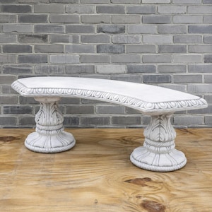 May include: A curved stone bench featuring a smooth, arched seat with a decorative rope-patterned border. The bench is supported by two ornate, pedestal-style legs that feature carved leaf motifs and a circular base with a rope-like trim detail.