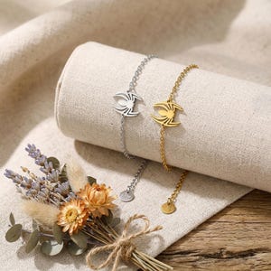May include: Two delicate chain bracelets, one in silver-tone and one in gold-tone metal, each featuring a central spider-shaped charm. Both bracelets include a small circular tag at the end of the chain, showcasing a polished and metallic finish.