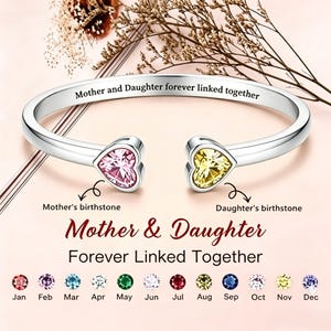 May include: A silver-toned open cuff bracelet featuring two heart-shaped gemstones, one pink and one yellow. The band is engraved with the text Mother and Daughter forever linked together. Below, a chart displays twelve birthstones by month.