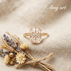 May include: A gold ring with a clear, rectangular gemstone featuring a starburst design. The ring is set on a neutral-coloured fabric, with dried flowers and the text "Amy art" in the background.