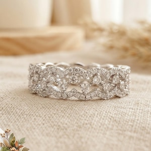 May include: A silver-toned eternity band ring featuring a double-layered, scalloped wave design. The entire surface of the metal is encrusted with numerous small, clear, round-cut stones that create a continuous, sparkling, and textured appearance.