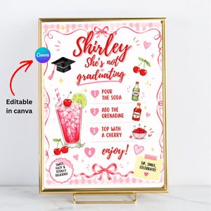 May include: A framed pink and gold print with the text "Shirley She's not graduating." The print includes illustrations of cherries, a cocktail, and instructions for a drink. The text "Sweet, fizzy & totally delicious!" is also included.