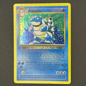 May include: A holographic Blastoise Pokémon card. The card features a blue and white Blastoise illustration with the text "Blastoise" and "100 HP". The card also includes text describing the Pokémon's abilities and stats. The card is 5' 3" long and weighs 189 lbs.