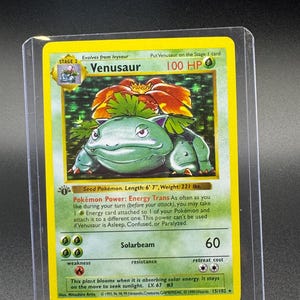 Puede incluir: Una carta coleccionable de Pokémon Venusaur, etapa 2, con un diseño verde y naranja. La tarjeta presenta el texto "Venusaur" y "100 HP". La tarjeta está en una funda protectora. La tarjeta mide 201 cm de largo y pesa 100 kg.