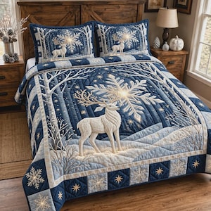 Puede incluir: Una colcha acolchada y dos fundas de almohada a juego con una escena de bosque invernal, ciervos blancos, grandes copos de nieve y árboles desnudos sobre un fondo azul oscuro, con un borde a cuadros y motivos de estrellas y copos.