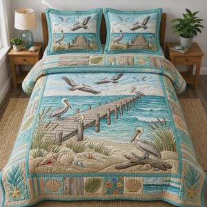 May include: A quilted bedspread and two matching pillow shams featuring a coastal scene with pelicans, a wooden pier extending into blue water, sandy beaches, seashells, and tall beach grass. The design includes light blue, tan, and brown tones.