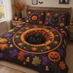Op de afbeelding: Een zwarte quilt en twee bijpassende kussenslopen met een Halloween-thema, voorzien van oranje pompoenen, paarse en oranje herfstbladeren, spinnenwebben en candy corn. Een zwarte kat staat centraal op de quilt en op een van de kussenslopen.