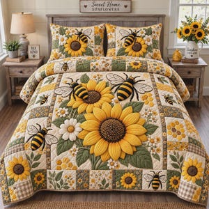 Op de afbeelding: Een doorgestikte sprei en twee bijpassende kussenslopen met een patroon van grote gele zonnebloemen, witte madeliefjes en zwart-gele bijen. Het ontwerp bevat honingraatmotieven en groen blad op een crèmekleurige achtergrond.