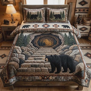 May include: A quilted bedspread featuring a central stone path leading into a cave, surrounded by pine trees and a large black bear in the foreground. Two matching pillow shams display black bears in a forest setting with a stone-like border.