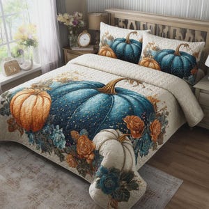 Op de afbeelding: Een doorgestikte sprei en twee bijpassende kussenslopen met een crèmekleurige achtergrond, voorzien van een grote centrale blauwgroene pompoen, een kleinere oranje pompoen en een witte pompoen, omringd door oranje en blauwe bloemaccenten en bladeren.
