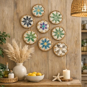 Könnte beinhalten: Neun runde Wanddekorationen mit Blumenmustern in verschiedenen Farben, die an einer Holzwand angebracht sind. Die Dekorationen haben gewebte Ränder. Eine Vase mit getrocknetem Gras, eine Schüssel mit Zitronen und eine Kerze stehen auf einem Holztisch.