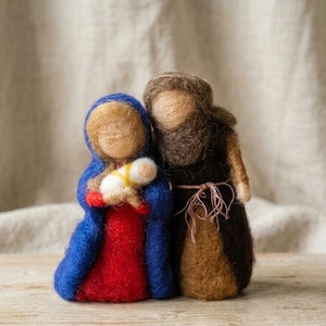 Pode incluir: Um conjunto de figuras de presépio em lã feltrada com duas personagens de pé, lado a lado. Uma figura usa uma capa azul sobre um vestido vermelho e segura um pequeno embrulho branco. A segunda figura usa uma túnica castanha escura.