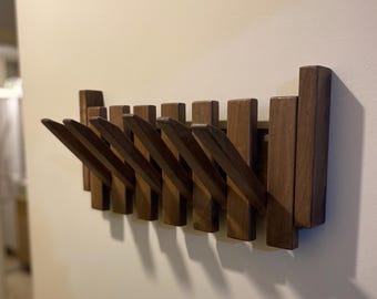 May include: A wall-mounted coat rack made of dark brown wood, featuring a series of vertical slats. Several of these slats are hinged to fold outward, functioning as hooks for hanging items, while others remain fixed in a vertical position.