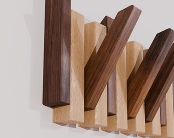 May include: A wall-mounted coat rack featuring a series of alternating rectangular wooden slats in dark walnut and light oak tones. The slats are arranged in a vertical pattern, with some pieces angled outward to function as hooks for hanging items.