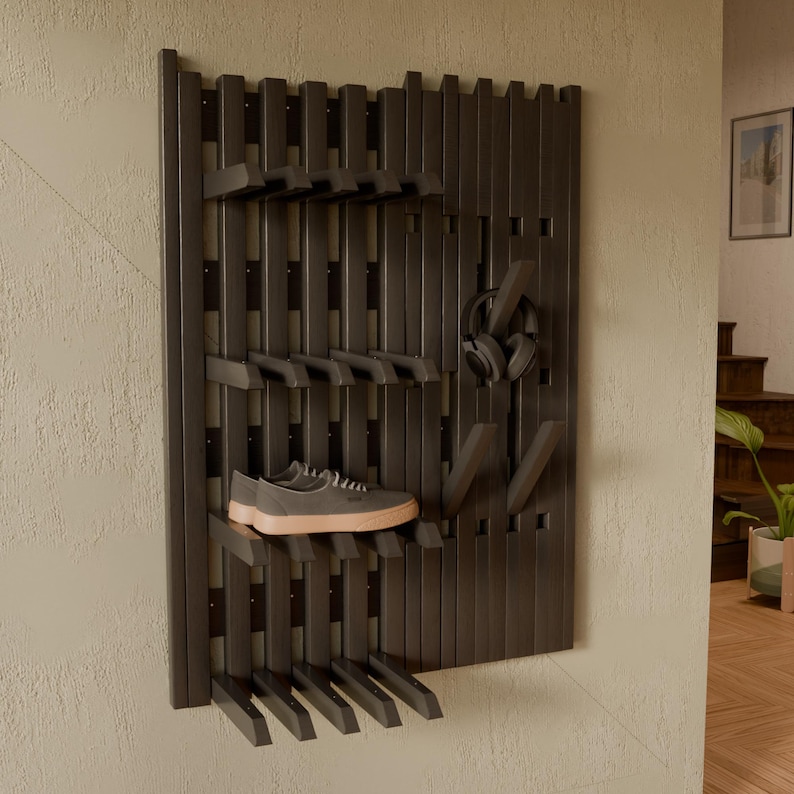 May include: A dark brown wall-mounted organizer rack featuring vertical slats and adjustable horizontal pegs. The rack holds a pair of gray sneakers with light-colored soles on one shelf and a pair of black over-ear headphones on a hook.