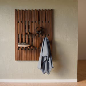 May include: A wall-mounted wooden slat organizer featuring vertical dark brown planks. The unit includes integrated hooks and shelves holding a pair of gray sneakers, a pair of black over-ear headphones, and a draped light blue fabric.