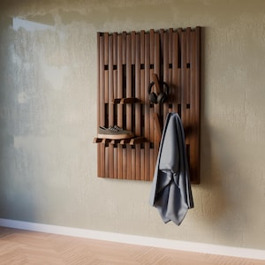 A dark walnut slatted wall rack with a gray shoe, black headphones, and a gray jacket hanging on it, against a light green wall.