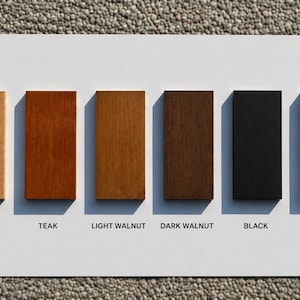 May include: A rectangular display board featuring six vertical wood color samples arranged in a row. The labels below each sample are Natural, Teak, Light Walnut, Dark Walnut, Black, and White, showing a range of wood tones and finishes.