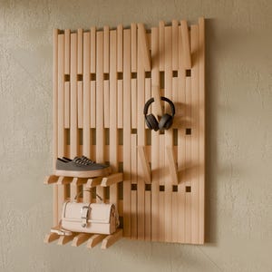 May include: A light-colored wooden wall-mounted organizer featuring vertical slats, integrated shelves, and protruding hooks. A pair of gray sneakers sits on the top shelf, a beige handbag rests on the bottom shelf, and black headphones hang from a hook.