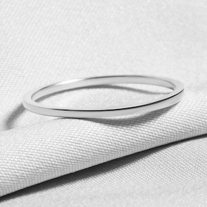 Könnte beinhalten: Ein dünner, silberfarbener Ring liegt auf einem strukturierten, hellgrauen Stoff. Der Ring ist kreisförmig und scheint aus Metall zu sein. Das Bild ist in Schwarzweiß gehalten und hebt das schlichte Design des Rings und die Textur des Stoffes hervor.
