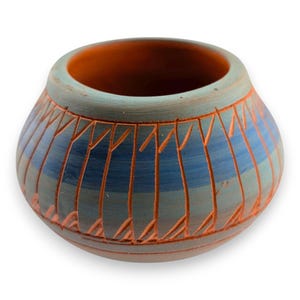 Puede incluir: Un cuenco de cerámica hecho a mano con forma redondeada. El exterior presenta una combinación de colores azul y gris con líneas grabadas en naranja. El interior es de un tono naranja cálido. Este cuenco decorativo es adecuado para la decoración del hogar.